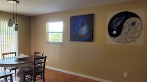 Un coin repas avec une table ronde, des chaises, une fenêtre et deux œuvres d’art accrochées au mur.