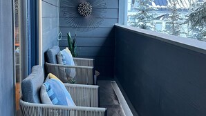 Un balcon agrémenté de fauteuils et de coussins en osier, un élément décoratif mural et une vue sur un paysage enneigé.