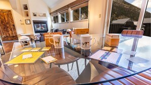 Un salon moderne doté d’une table à manger au plateau en verre, de sièges en cuir, d’une cheminée et offrant une vue imprenable sur les montagnes.