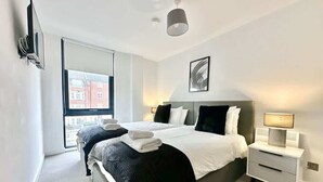 Ein modernes Schlafzimmer mit zwei Betten, einem großen Fenster, einem Flachbildfernseher und einer Nachttischlampe.