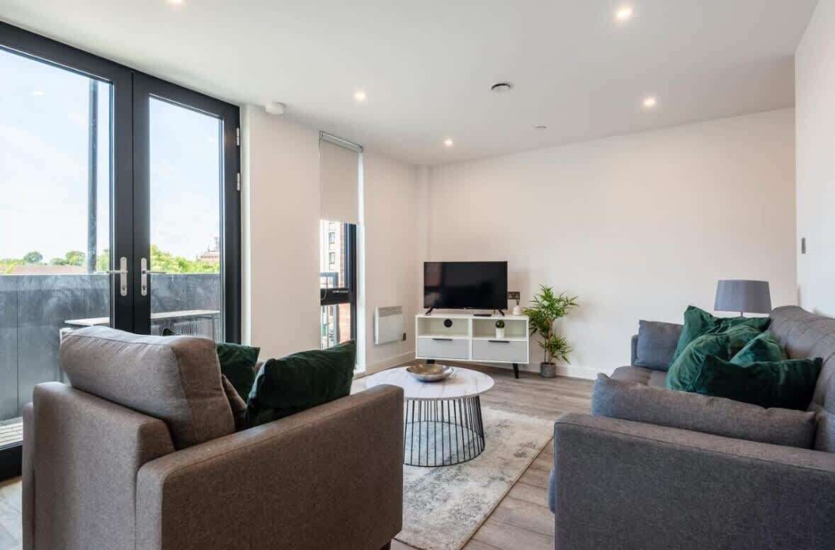 A modern living room with a sofa, a coffee table, a TV, and a sliding glass door leading to an outdoor area.