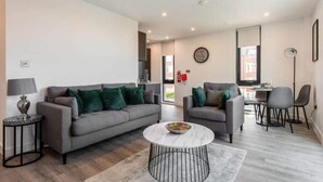 Ein modernes Wohnzimmer mit grauem Sofa, einem runden Couchtisch und einem Essbereich mit Stühlen und Tisch.