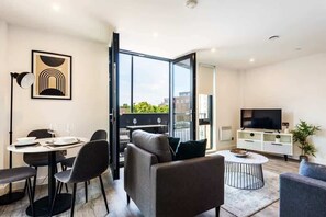 A modern living room with a dining area, a sofa, a coffee table, and a TV. - Stunning Apartment With Balcony Walking Distance (York)