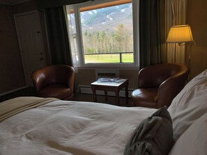A hotel room with a bed, two leather chairs, a small table, a lamp, and a window with a view of a green landscape and mountains. - Ledgerock at Whiteface -Standard Double Room (Wilmington)