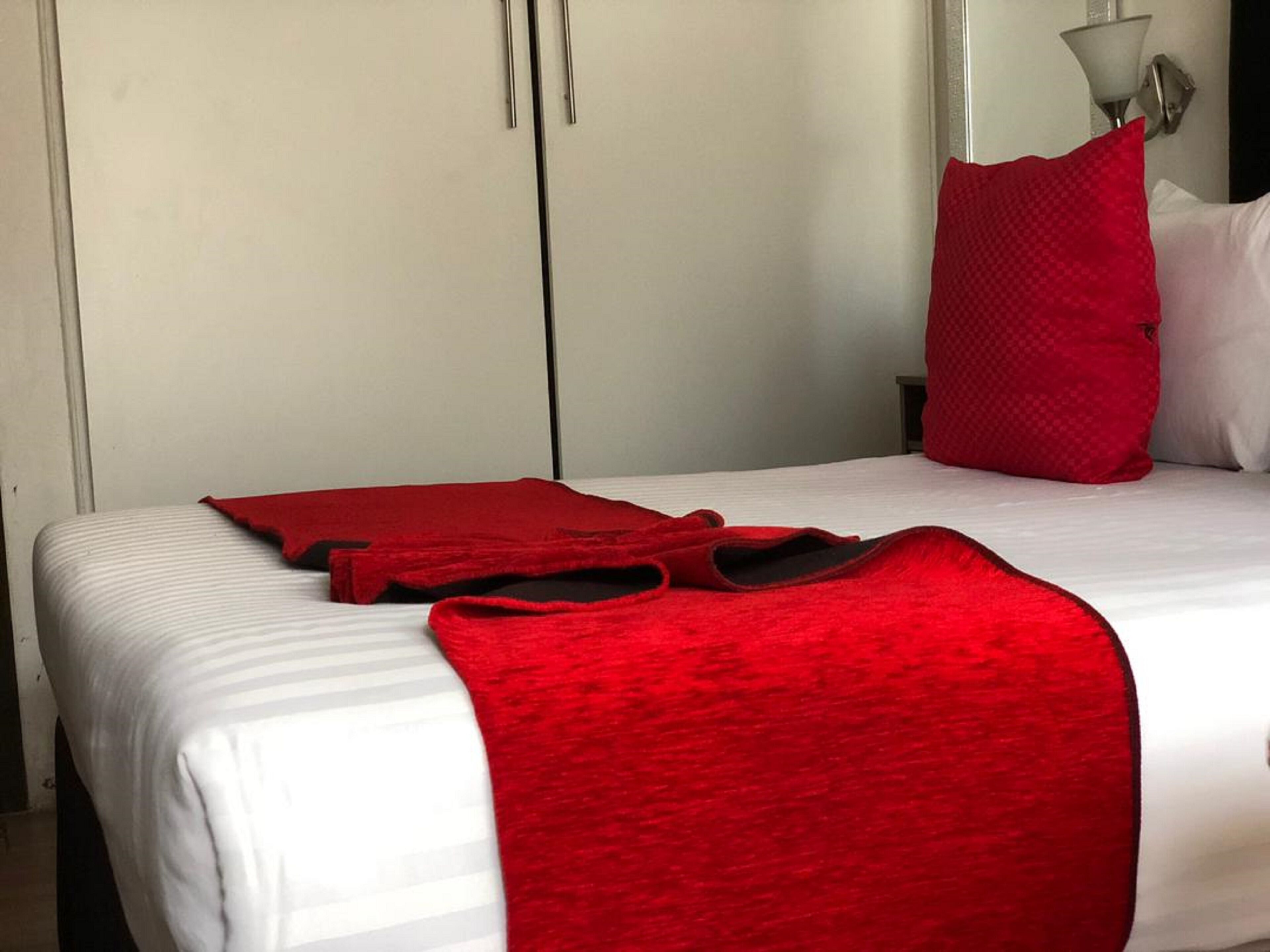 Una habitación de hotel con una cama, una manta roja y una almohada roja.