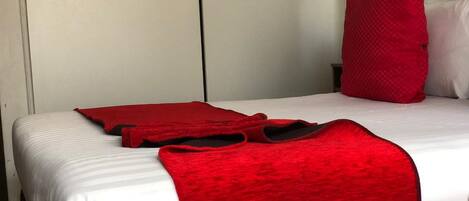 Una habitación de hotel con una cama, una manta roja y una almohada roja.