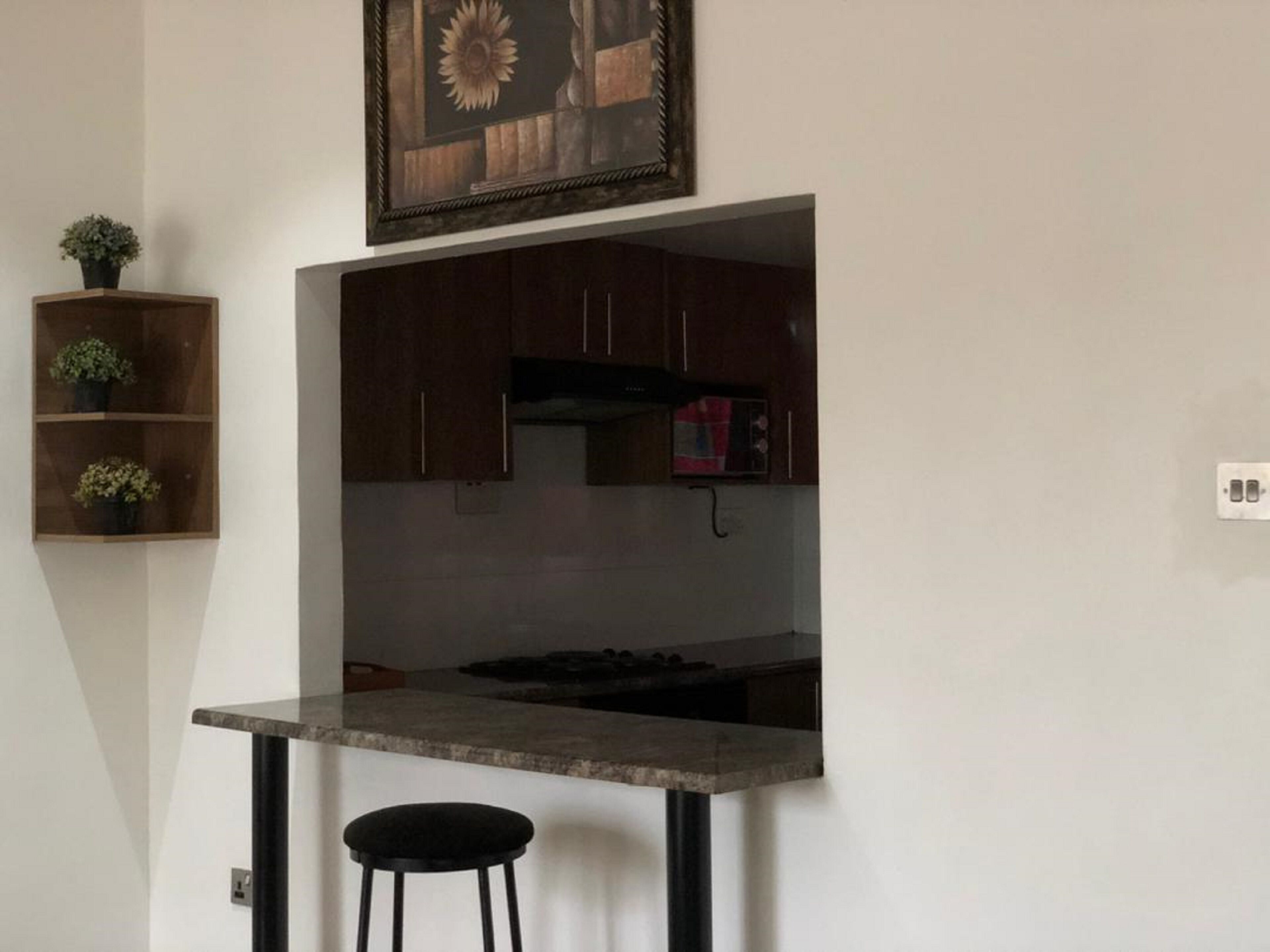 Una cocina compacta con armarios de madera oscura, un microondas integrado y un mostrador pequeño con un taburete.