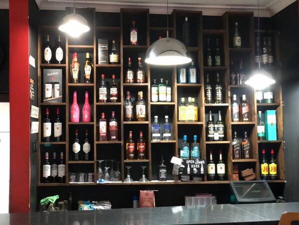 A bar area with shelves stocked with various bottles of alcohol, a sign indicating 'OPEN BEER HERE', and a counter with a cash register.