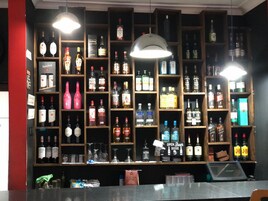 A bar area with shelves stocked with various bottles of alcohol, a sign indicating 'OPEN BEER HERE', and a counter with a cash register.
