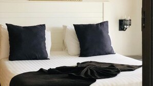 Habitación de hotel con una cama, dos almohadas, una mesita de noche, una lámpara de pared y una mosquitera colgante.