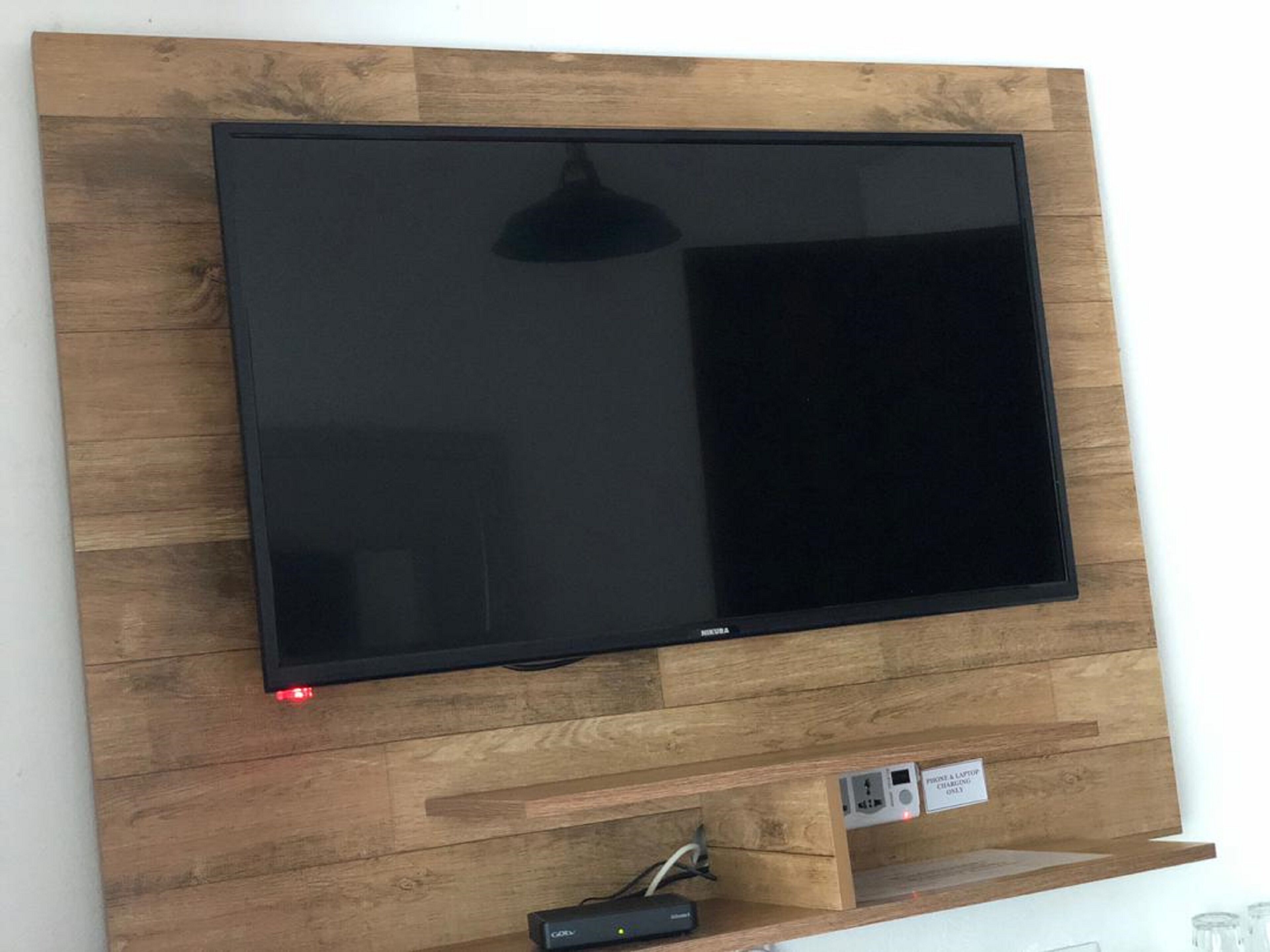 Un televisor de pantalla plana montado en una pared de madera con un estante debajo.