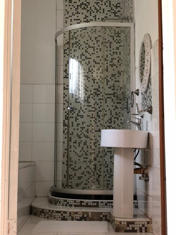 A shower with mosaic tile walls, a white sink, and a mirror. - Rosewood place Lodge (Kitwe)