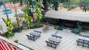 Un patio al aire libre con varias bancas y mesas de madera, rodeado de follaje y una zona de estar cubierta.