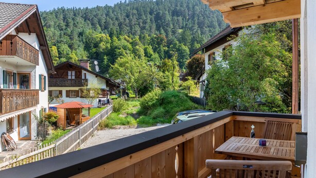 A wooden balcony with a table and chairs, overlooking a forested hillside. - Apartment 'Josef' with Mountain View, Shared Garden and Wi-Fi (Garmisch-Partenkirchen)