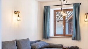 A modern living room with a grey sofa, a wooden side table, and a window with curtains. - Apartment 'Josef' with Mountain View, Shared Garden and Wi-Fi (Garmisch-Partenkirchen)