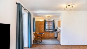A modern kitchen with wooden cabinets, a dining area with a table and chairs, and a TV on the left. - Apartment 'Josef' with Mountain View, Shared Garden and Wi-Fi (Garmisch-Partenkirchen)