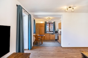 A modern kitchen with wooden cabinets, a dining area with a table and chairs, and a TV on the left.