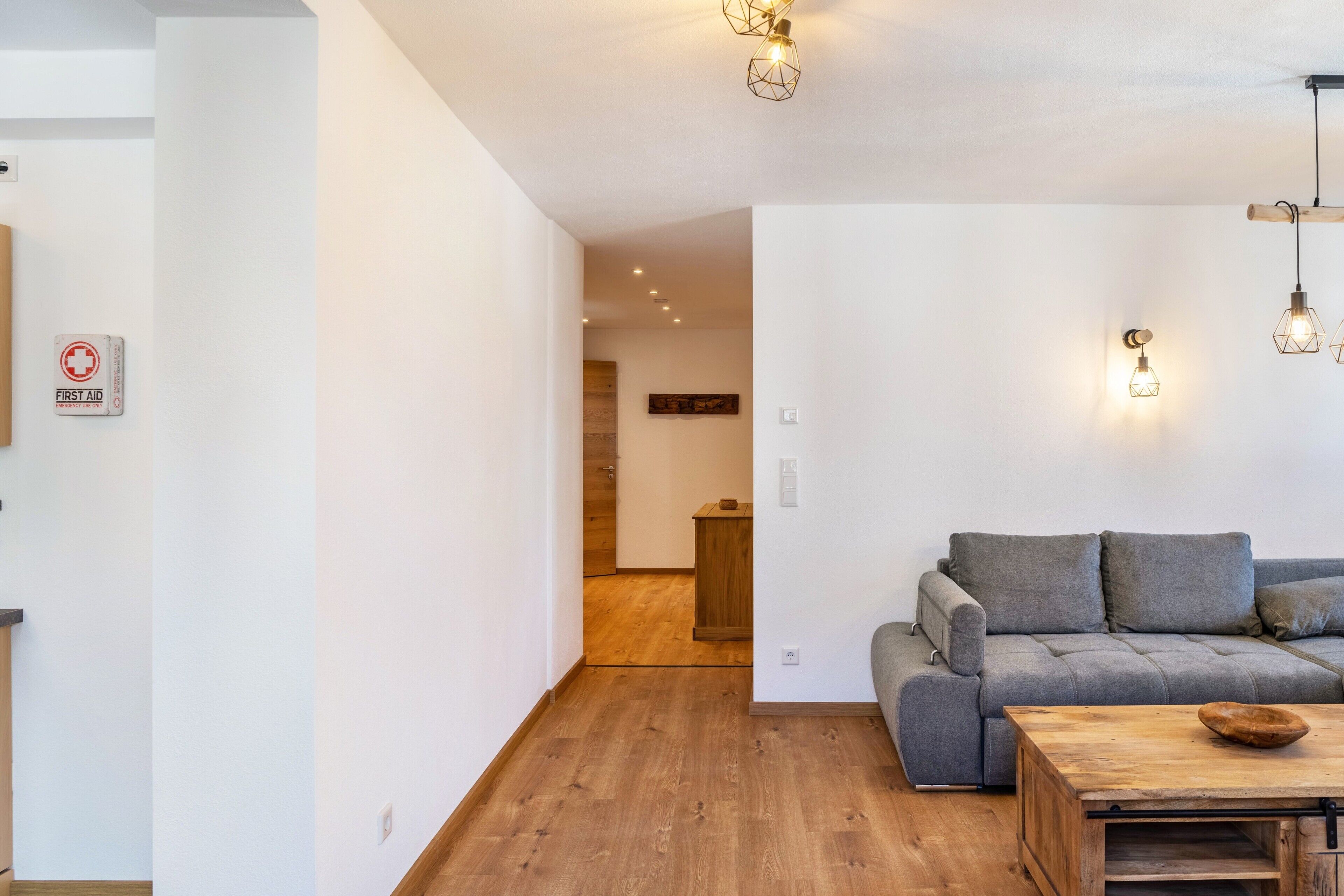 Een moderne woonkamer met een grijze bank, houten vloer en hanglampen.