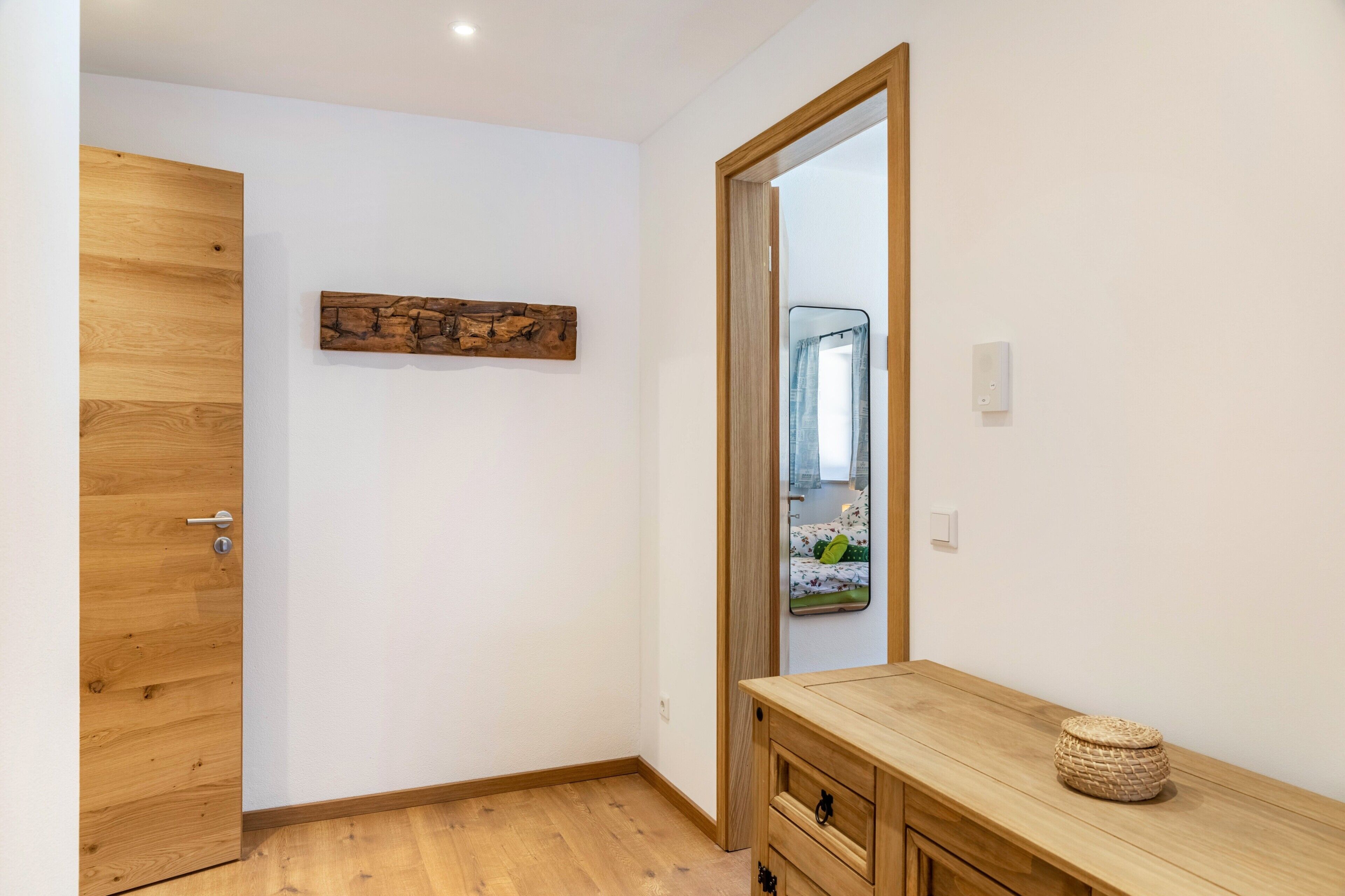 Een kamer met een houten deur, een spiegel, een houten dressoir en een kunstwerk aan de muur.