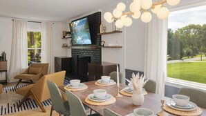 A modern living room with a fireplace, a television, and a dining area set for four. - 4BR Pineville Retreat - Private Pool - Fire Pit - Near Carowinds & Charlotte (Pineville)