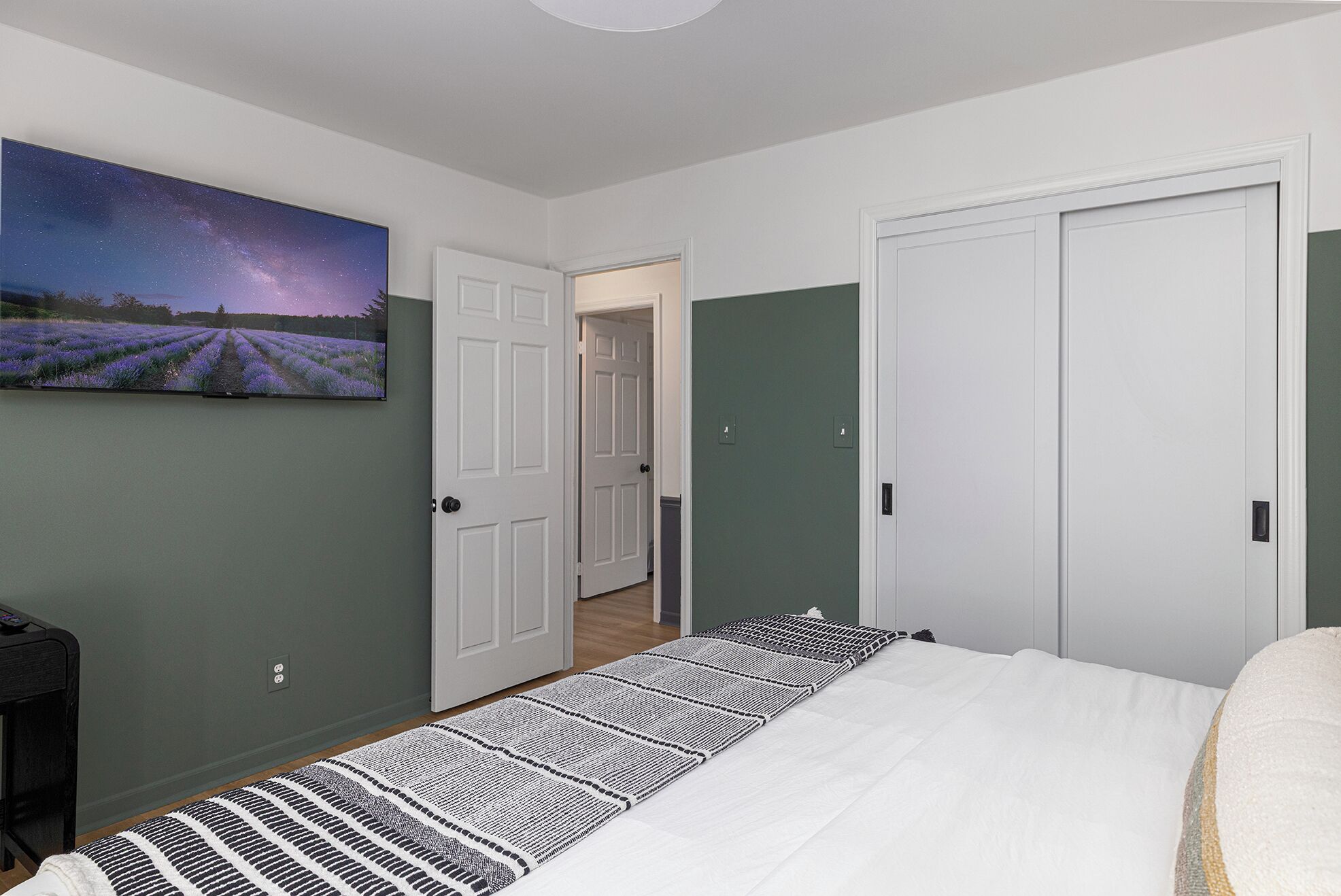 A bedroom with a bed, a painting of a lavender field, and two doors.