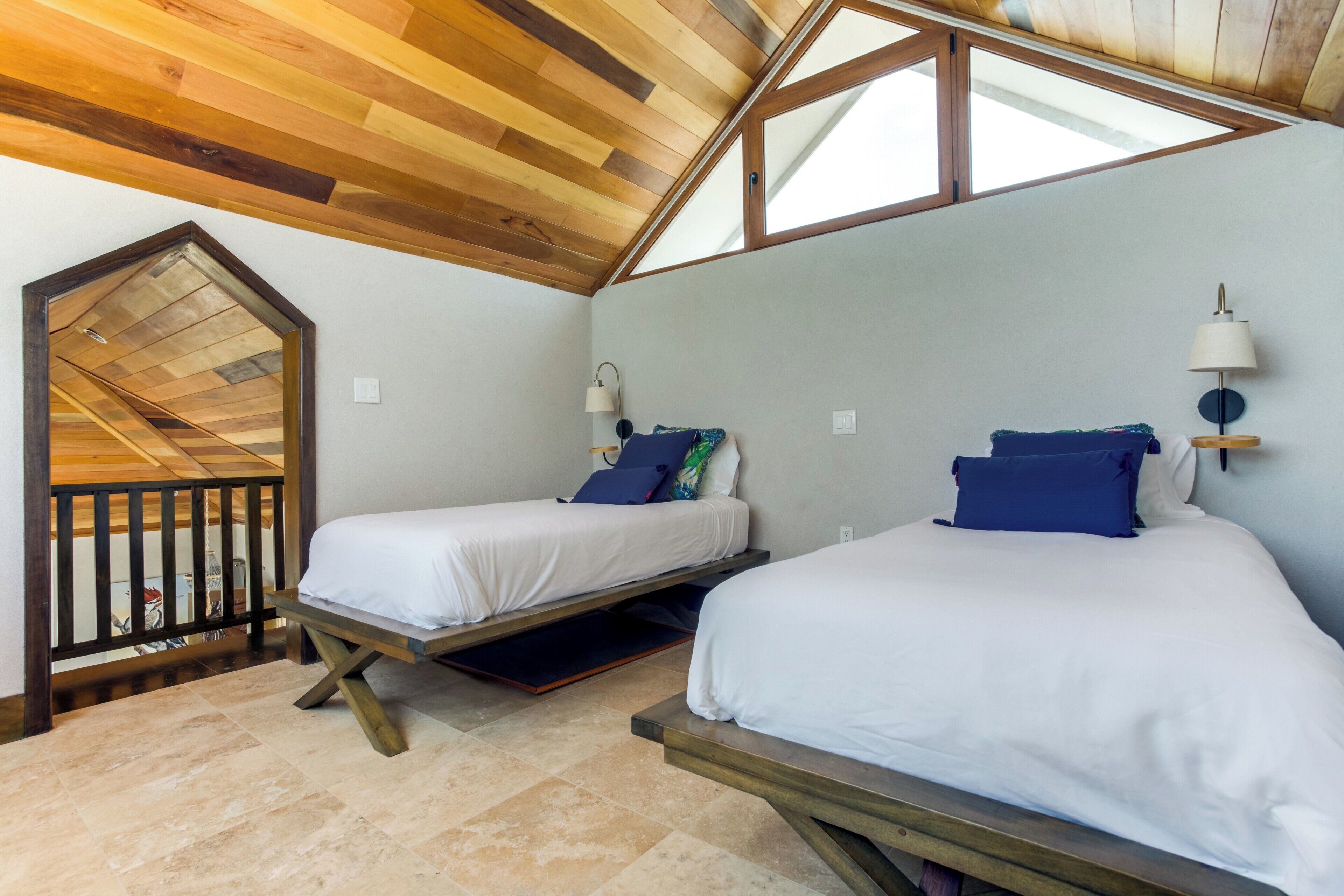A room with two beds, a skylight, wooden ceiling beams, and a small balcony.