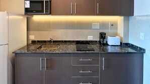 Una cocina moderna con armarios oscuros, un lavamanos de acero inoxidable, un microondas, un tostador y una cafetera.