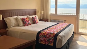 Ein Hotelzimmer mit einem großen Bett, einem Schreibtisch und Meerblick aus dem Fenster.