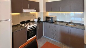 Una cocina compacta con armarios oscuros, estufa a gas, microondas y horno empotrado.
