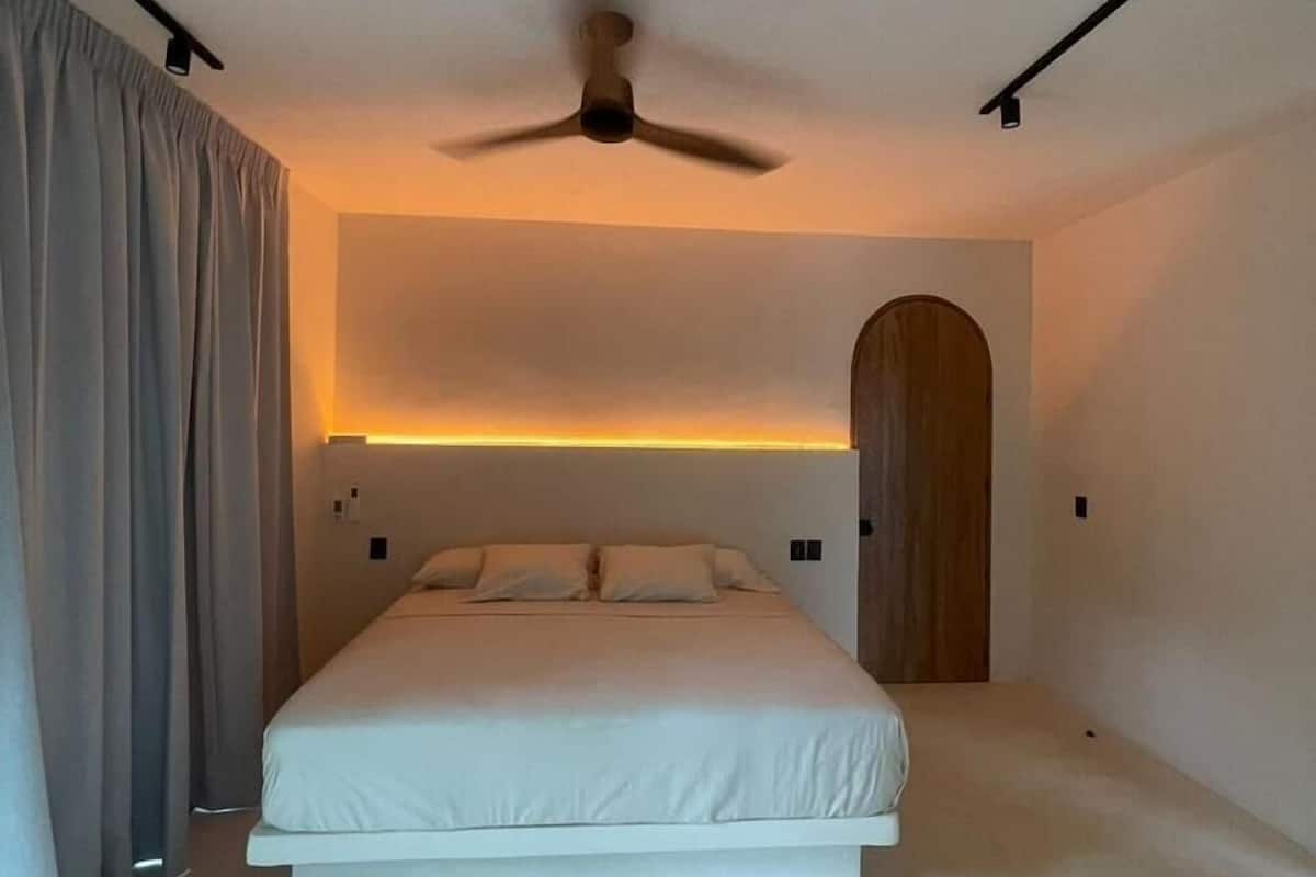A modern bedroom with a bed, ceiling fan, and a wooden door.