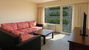 Een woonkamer met een bloemenbank, een salontafel en een tv op een houten dressoir.