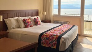 A hotel room with a large bed, a desk, and a view of the sea through the window.