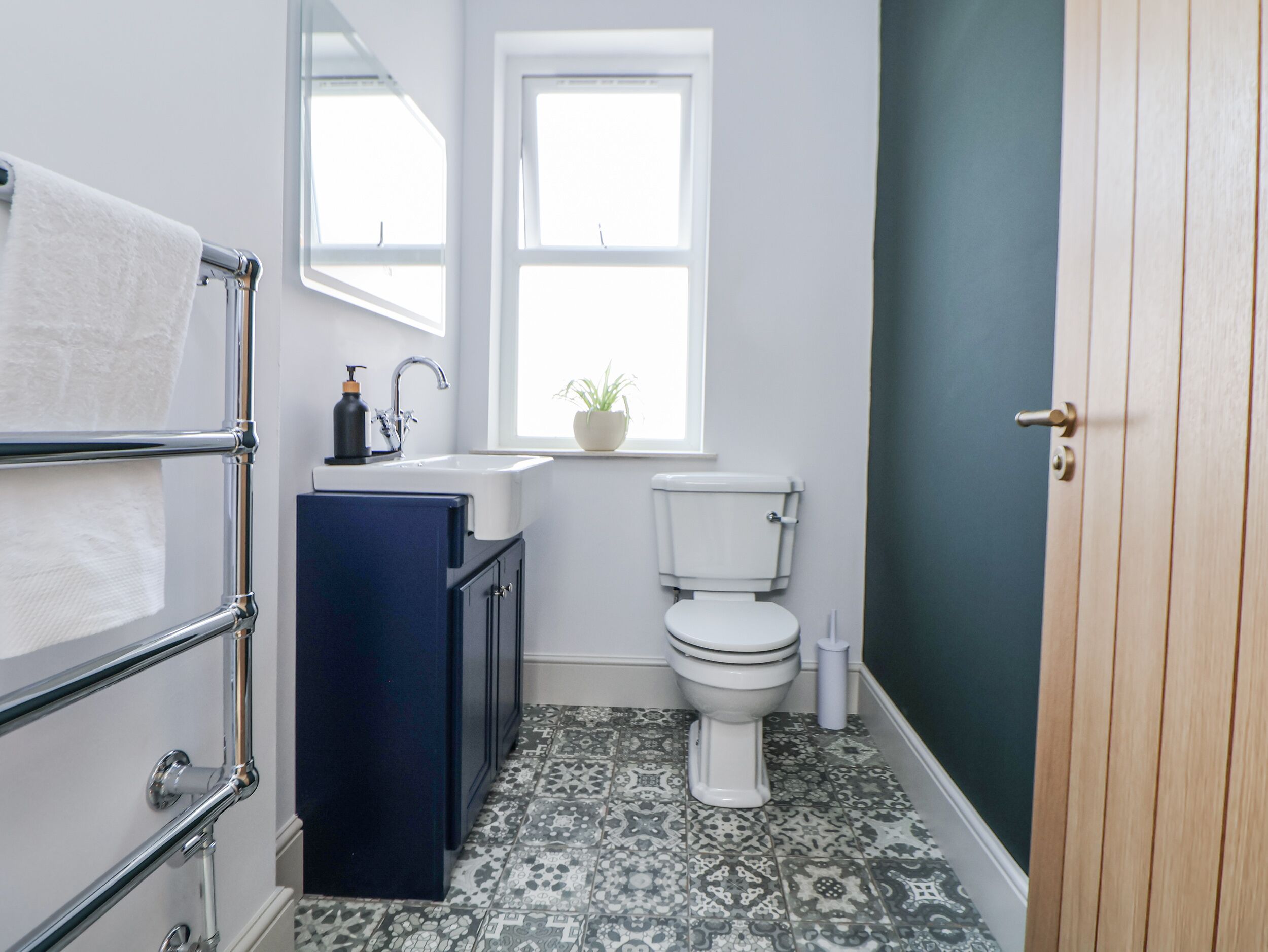 Et badeværelse med toilet, vask, håndklædetørre og et vindue med en plante.