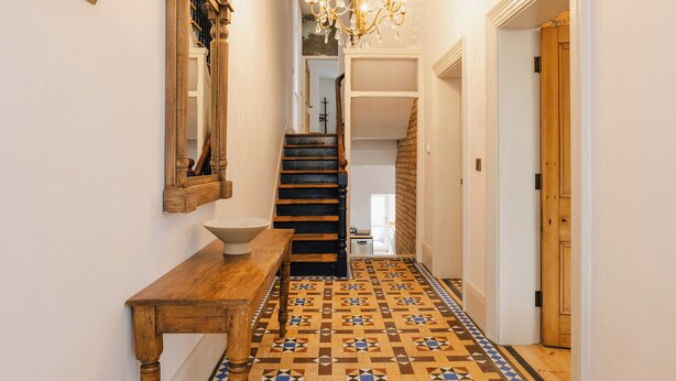 Un couloir avec un banc en bois, un sol à motifs, un lustre et un escalier menant à une autre pièce.