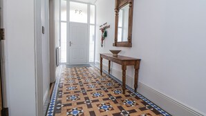 Un couloir avec des carreaux de sol à motifs, une porte blanche et une console en bois sur laquelle est posé un bol.