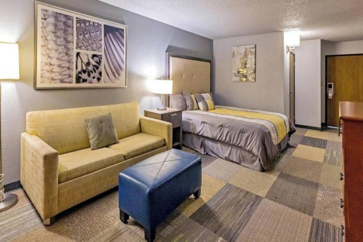 A hotel room with a bed, a sofa, a small table, and a wall-mounted artwork.