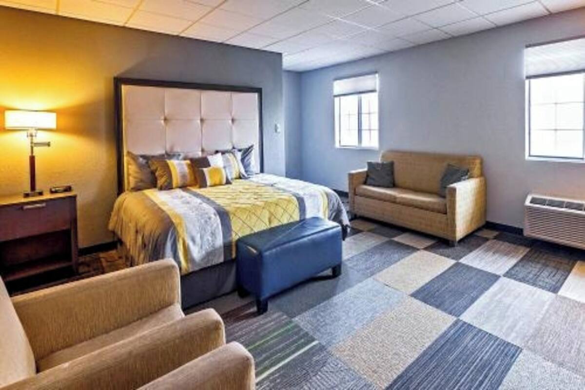 A hotel room with a bed, a sofa, a chair, a lamp, and a window.