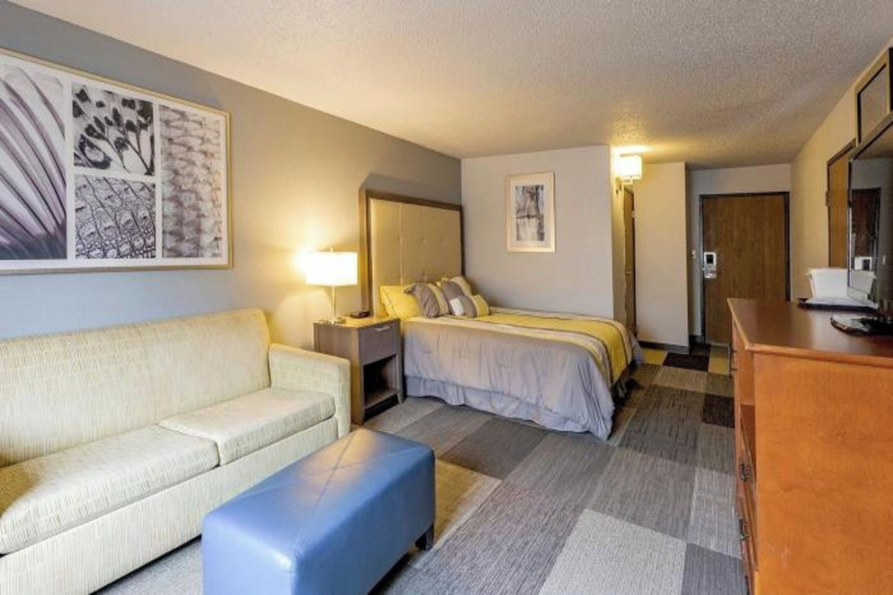 A hotel room with a bed, a sofa, a desk, and a large painting on the wall.