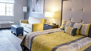 Habitació d'hotel amb un llit gran, un sofà, una tauleta de nit, una làmpada i una obra d'art penjada a la paret.