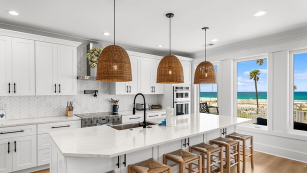 A modern kitchen with white cabinetry, a large island with bar stools, and a view of the beach. - Luxury Gulf-front Retreat | Sleeps 24 | Private Pool (Port St. Joe)