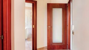 A hallway with two wooden doors, one with a frosted glass panel, and a light switch on the wall.