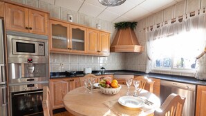 A modern kitchen with wooden cabinets, stainless steel appliances, and a dining area with a fruit bowl and wine glasses. - Private Paradise in Fuerteventura · Pool, Barbecue, and Dream Beaches (CN)