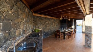 A rustic kitchen with stone walls, a wooden ceiling, and a dining area with a long table and chairs. - Private Paradise in Fuerteventura · Pool, Barbecue, and Dream Beaches (CN)