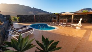 A pool area with lounge chairs, a pool, and a stone wall. - Private Paradise in Fuerteventura · Pool, Barbecue, and Dream Beaches (CN)