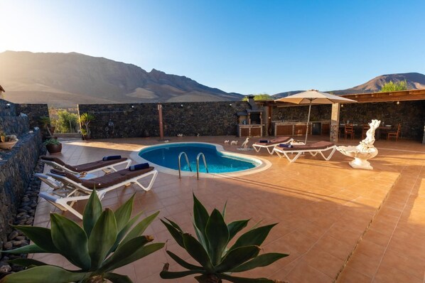 Zona de piscina con sillones de descanso, piscina y pared de piedra.