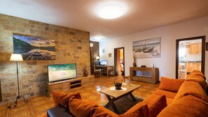 A living room with a stone wall, a flat-screen TV, orange sofas, and a wooden coffee table. - Private Paradise in Fuerteventura · Pool, Barbecue, and Dream Beaches (CN)