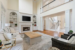 Amplia sala de estar con chimenea, muebles blancos y una escalera que conduce a un nivel superior.