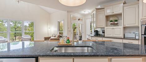 A spacious kitchen with a granite countertop, white cabinetry, and a large island with a sink.