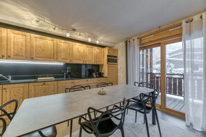 A kitchen with wooden cabinets, a dining table, chairs, and a view of a snowy landscape through a sliding glass door.
