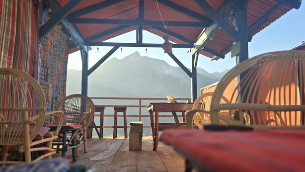 Une terrasse en bois, agrémentée de chaises et d’une table en osier, qui offre une vue sur un paysage montagneux.